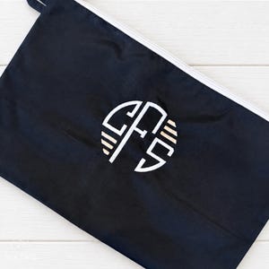 May include: A black rectangular zippered pouch featuring a white circular monogram logo in the center. The logo consists of the letters CFS stylized with horizontal lines on the sides. The pouch has a white zipper closure along the top edge.