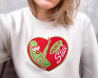 May include: White sweatshirt with a red heart-shaped design featuring a green pickle with a face and the text "PICKLE SLUT" in a green oval.