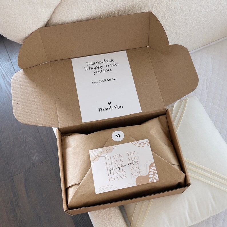 May include: An open cardboard box with a white label that reads "This package is happy to see you too." and "Thank You." Inside, the contents are wrapped in brown paper. A small card with "Thank You" is also visible.