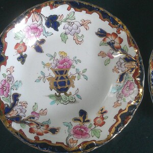 May include: Two vintage porcelain bowls with blue and gold trim and floral patterns. The bowls have a white background with colorful flowers and a central design of a vase with flowers.