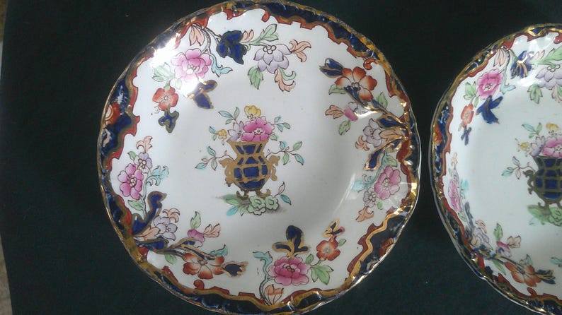May include: Two vintage porcelain bowls with blue and gold trim and floral patterns. The bowls have a white background with colorful flowers and a central design of a vase with flowers.