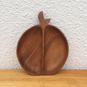 May include: A wooden serving dish shaped like an apple with two divided sections. The dish is made of dark brown wood and has a natural finish.