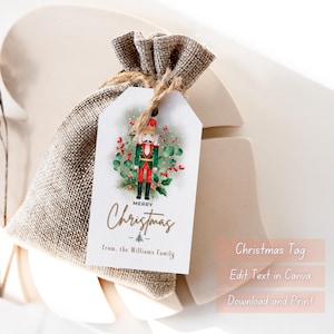 Könnte beinhalten: Ein Weihnachtsgeschenkanhänger mit einer Illustration eines Nussknackers, umgeben von Grün und Beeren. Der Anhänger ist mit einer Schnur an einem Jutesack befestigt. Der Anhänger lautet "Merry Christmas" und "from, the Williams Family".