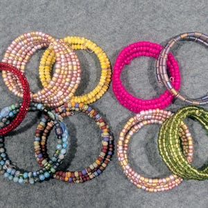 May include: A collection of spiral bracelets in various colors, including red, pink, yellow, blue, and green. The bracelets are made of small beads and are arranged in a circular pattern. The bracelets are a fashionable accessory.