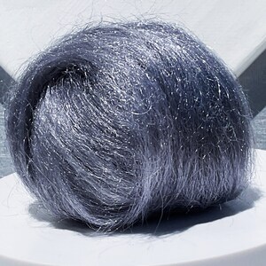 May include: A ball of blue-grey yarn with a metallic sheen. The yarn is tightly wound, creating a dense, textured sphere. The fibers catch the light, giving it a shimmering appearance. Ideal for knitting or crochet projects.