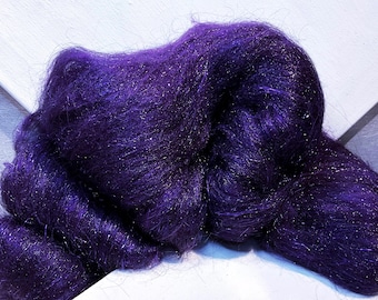 May include: A close-up of a mass of deep purple fiber with shimmering silver strands. The fiber is tightly packed and appears soft and fluffy, with a slight sheen. The background is a white surface.
