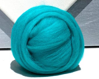 Könnte beinhalten: Ein Ball aus lebendigem teal-farbenem Wollvlies. Die Wolle ist eng gewickelt und bildet eine dichte, runde Form. Die Textur erscheint weich und flauschig, mit sichtbaren Fasern. Der Hintergrund ist eine Mischung aus Weiß und Grau, die einen Kontrast zum hellen Teal bildet.