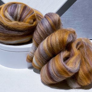 May include: Two balls of colorful wool yarn in shades of brown, orange, and white. The yarn is arranged in a loose, swirling pattern.