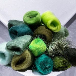 Könnte beinhalten: Eine Sammlung von gerollten Wollvliesstücken in verschiedenen Grüntönen, darunter Limettengrün, Waldgrün, Oliv und Minze. Die Fasern haben eine weiche, flauschige Textur, wobei einige Stücke einen dezenten metallischen Schimmer und andere ein mattes Finish aufweisen.