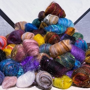 May include: A large pile of small, rounded bundles of multi-colored wool roving. The fibers feature a variety of vibrant hues including red, blue, purple, yellow, and black, many interwoven with metallic, shimmering threads throughout the texture.