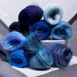 May include: A collection of wool roving bundles in various shades of blue, ranging from deep navy and midnight blue to bright azure, sky blue, and pale powder blue. Several of the fiber bundles feature integrated silver metallic fibers.