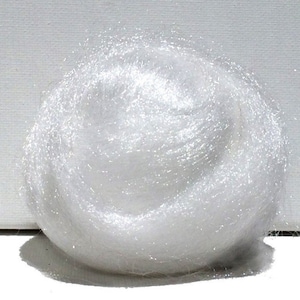 May include: A ball of white, shiny fiber material, possibly for crafting or decorative purposes. The fibers are tightly wound, creating a dense, cloud-like shape. The material has a soft, delicate appearance.