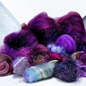 May include: A collection of purple and violet yarn in various forms, including loose fiber, rolled balls, and a cylindrical shape. Some yarn has a sparkly, glittery appearance, adding a touch of shimmer. The assortment is suitable for fiber art and crafting projects.