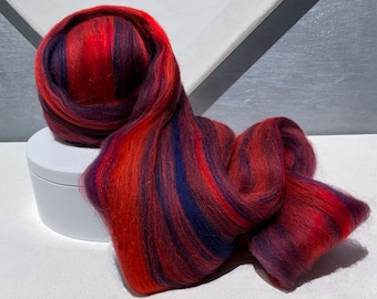 May include: Red, purple and blue wool roving in a striped pattern. The roving is arranged in a loose, flowing shape.
