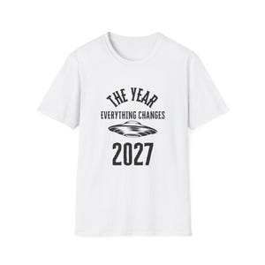 May include: White t-shirt with a black graphic design. The design includes the text "THE YEAR EVERYTHING CHANGES" above an image of a flying saucer, with the year "2027" below the saucer.