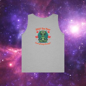 May include: A gray tank top with a graphic of a green alien meditating, surrounded by hearts. The text "2027 The Year Everything Changes" is above and below the alien. The background is a purple and blue galaxy.