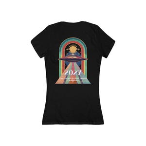 Może przedstawiać: Czarny t-shirt z grafiką w stylu retro przedstawiającą UFO nad tęczowym łukiem, słońcem i gwiazdami. Grafika zawiera rok "2027" i tekst "THE YEAR EVERYTHING CHANGES".
