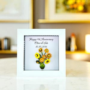 May include: A framed artwork with a white border, featuring a floral arrangement. The artwork displays a bouquet of yellow and orange flowers in a green vase. Text reads "Happy 9th Anniversary Oliver & Isla 10.10.2016".