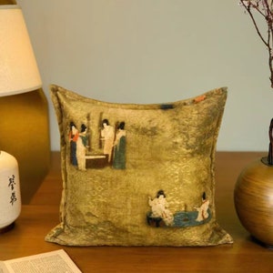 Op de afbeelding: Een vierkant kussen met een gouden achtergrond en een vintage print van mensen in traditionele kleding. De print is in tinten bruin, rood en blauw.