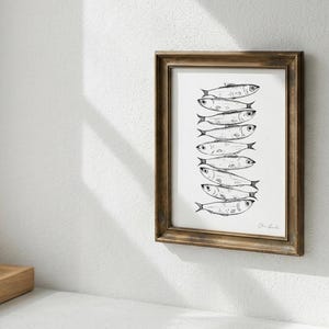 Puede incluir: Una pieza de arte mural enmarcada que presenta una ilustraci&oacute;n en tinta negra y blanca de una pila vertical de ocho peces. La obra est&aacute; encerrada en un marco de madera marr&oacute;n oscuro con un perfil cl&aacute;sico, mostrando el detallado trazo de los peces.