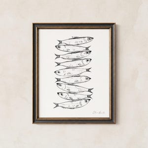 Puede incluir: Una ilustraci&oacute;n en tinta negra y blanca enmarcada que presenta una pila vertical de nueve peces. Los peces est&aacute;n dibujados en un estilo lineal detallado, orientados horizontalmente y superpuestos uno sobre otro. La obra est&aacute; en un marco oscuro.