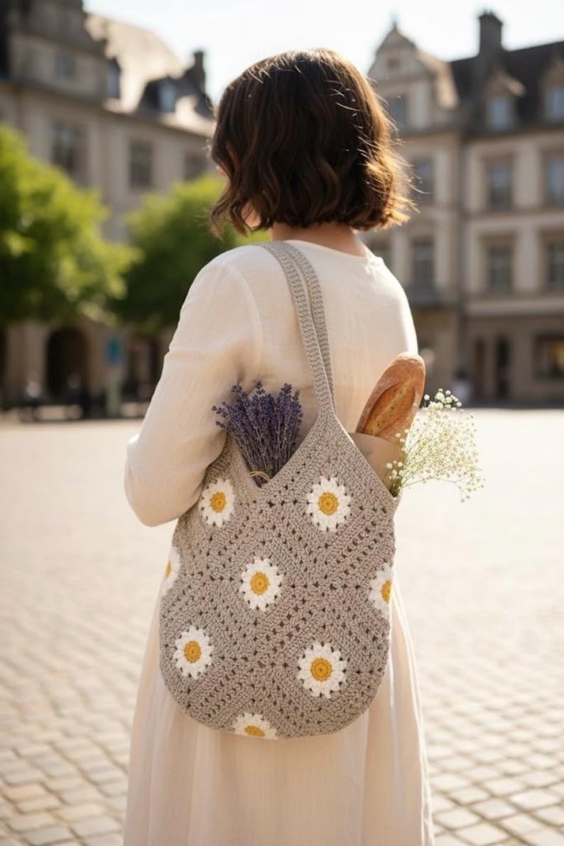 Puede incluir: Bolso tote de crochet gris con estampado de margaritas, llevado al hombro. El bolso contiene una baguette, lavanda y flores blancas. El bolso est&aacute; hecho de hilo suave y tiene un asa resistente.