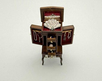 May include: A miniature wooden jewelry armoire with multiple compartments and drawers. The armoire is open, revealing a red velvet interior and various pieces of jewelry, including necklaces, rings, and a decorative fan. The armoire is on four curved legs.
