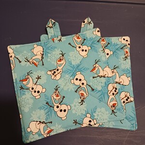 May include: Two blue quilted pot holders with a pattern of Olaf from Frozen. The pot holders have a snowflake design and are perfect for protecting your hands from hot dishes.