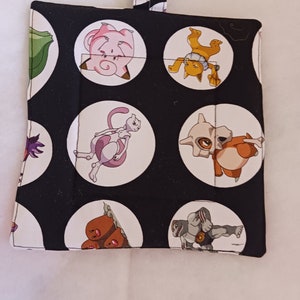 May include: Black fabric hot pad with white circles featuring cartoon images of Pokemon characters.