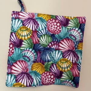 May include: A colorful pot holder with a seashell pattern. The pot holder is made of fabric and has a loop for hanging.