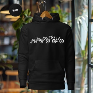Può includere: Felpa con cappuccio nera con una grafica bianca di una linea di biciclette di diverse dimensioni, da una piccola bicicletta per bambini a una grande mountain bike.