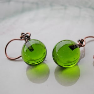 May include: A pair of green glass ball earrings with copper wire hooks. The glass balls have a slightly textured surface and contain small air bubbles.