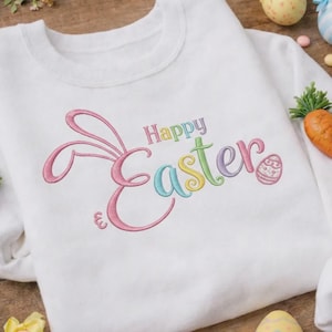 May include: White sweatshirt with embroidered "Happy Easter" text in pastel colors. The design includes bunny ears and an Easter egg. The sweatshirt is a crew neck style, perfect for spring or Easter celebrations.