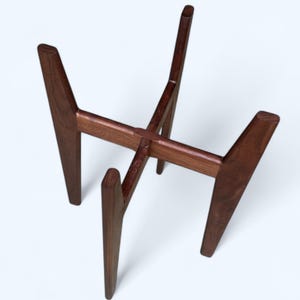 May include: A dark brown wooden plant stand with a mid-century modern design. The stand has four angled legs and a cross-shaped support structure. The stand is approximately 12 inches tall and 10 inches wide.