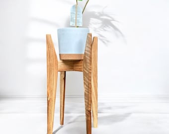 May include: A light blue ceramic planter sits on a wooden plant stand with four legs. The stand is made of natural wood with a light brown finish. The plant stand is approximately 30 inches tall.