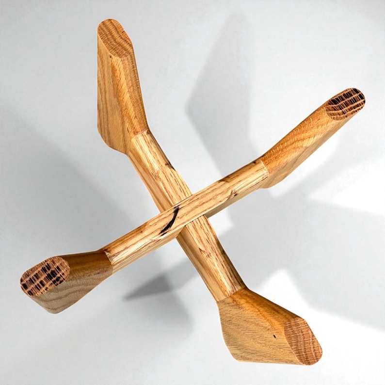 May include: A handcrafted wooden object with an X-shaped design. The natural wood has a light brown color with visible grain patterns. The ends are wider and angled, creating a unique aesthetic. The object appears to be a decorative piece.