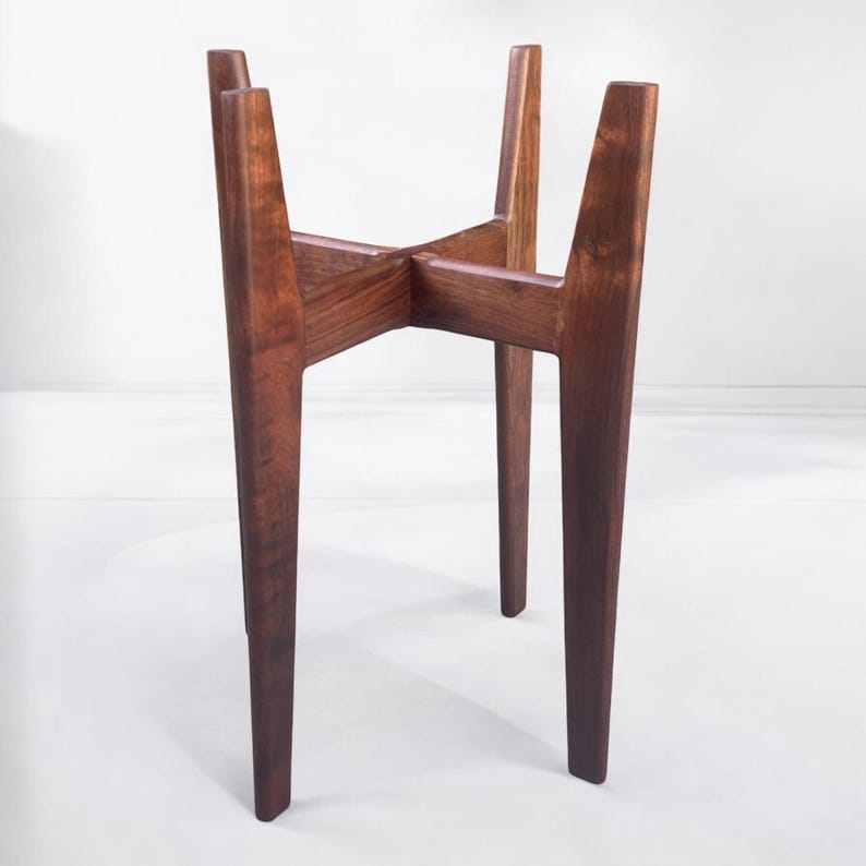 May include: A wooden plant stand with a mid-century modern design. The stand is made of dark brown wood and features four angled legs that intersect at the center. The legs are tapered and create a stable base for a potted plant.