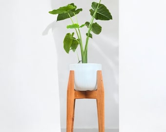 以下が含まれることがあります： 白いプランターに緑の植物が植えられており、4本の脚が付いた木製プランタースタンドの上に置かれています。プランタースタンドは天然木で作られており、シンプルなデザインです。