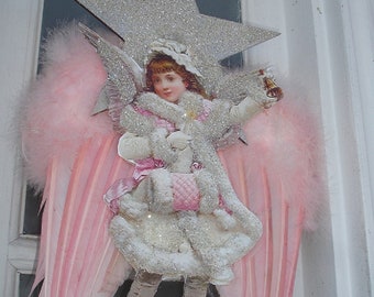 May include: A vintage Christmas angel ornament with pink feathered wings, a silver glitter star, and a white dress with a pink sash.
