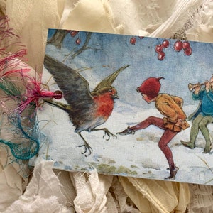 Puede incluir: Una tarjeta de Navidad vintage con un petirrojo posado en un paisaje nevado con dos niños. Un niño está tocando una flauta mientras el otro patea al pájaro. La tarjeta tiene un fondo azul con bayas rojas y un primer plano blanco nevado.