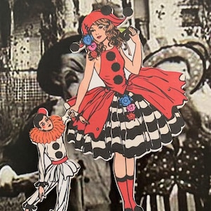 May include: A hanging ornament featuring a central figure in a red dress with black polka dots and a black and white striped skirt, holding the hand of a smaller clown figure wearing a white outfit with a red ruffled collar and black accents.