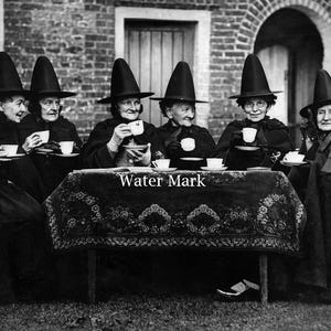 May include: A black and white photograph of eight individuals wearing tall, pointed black hats and dark cloaks, seated around a rectangular table covered with a patterned cloth. Each individual holds a white teacup and saucer. The text Water Mark is visible on the table cloth.