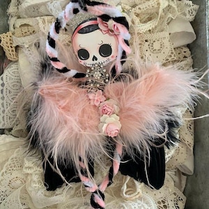 May include: A pink and black angel ornament with a skull face, pink feathers, and a pink and white striped halo.