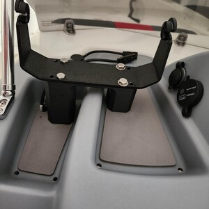 May include: A black metal bracket with two vertical supports and a horizontal bar. The bracket is mounted on a grey surface and has several screws and bolts. The bracket is designed to hold a device, such as a fish finder or GPS unit.
