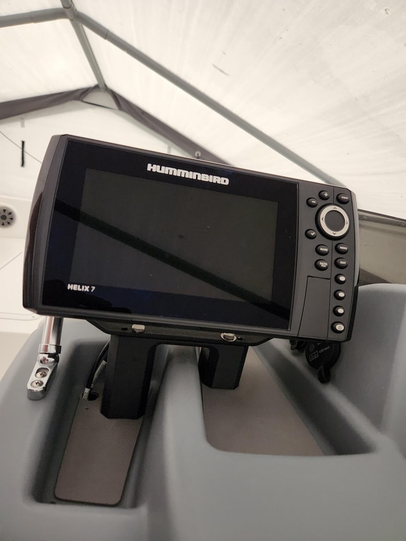May include: A black Humminbird HELIX 7 fish finder mounted on a grey surface. The fish finder has a black and white screen and a variety of buttons.