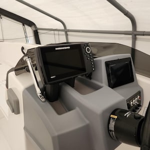 May include: A black Humminbird HELIX 7 fish finder mounted on a boat dashboard. The fish finder has a black and white screen with a grey bezel. The screen displays the Humminbird logo and the text "HELIX 7".