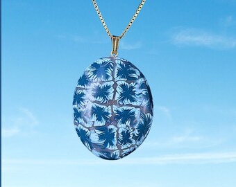 Könnte beinhalten: Eine goldene Kettenkette mit einem ovalen Anhänger mit blau-weißem Muster. Der Anhänger hat ein geometrisches Design mit einem floralen Motiv.