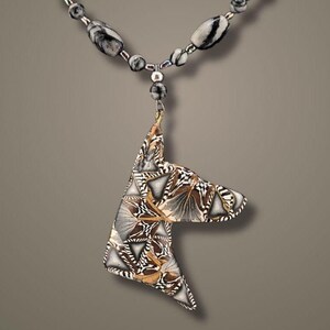 May include: A silver necklace with black and white patterned beads and a pendant shaped like a dog's head. The pendant is made of black, white, and gold patterned clay.