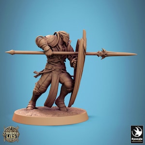 May include: A miniature figurine of a warrior in armor, holding a spear and shield. The figure is painted in a brown color and is standing on a round base.