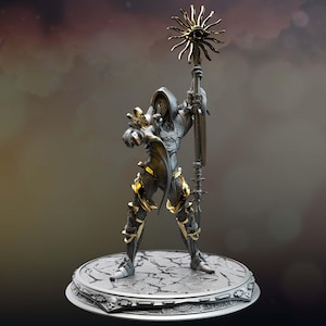 Può includere: Una statuetta in argento e oro di una figura incappucciata che tiene uno scettro con un designo solare. La figura è in piedi su una base circolare con un design di pietra screpolata.